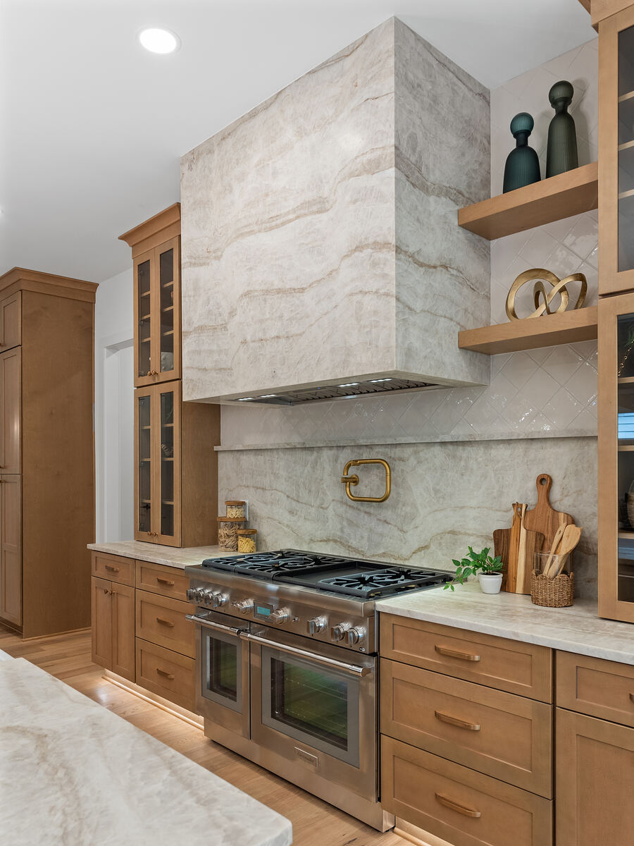 Oak kitchen cabinetry with a marble slab hood, brass pot filler, and a professional range