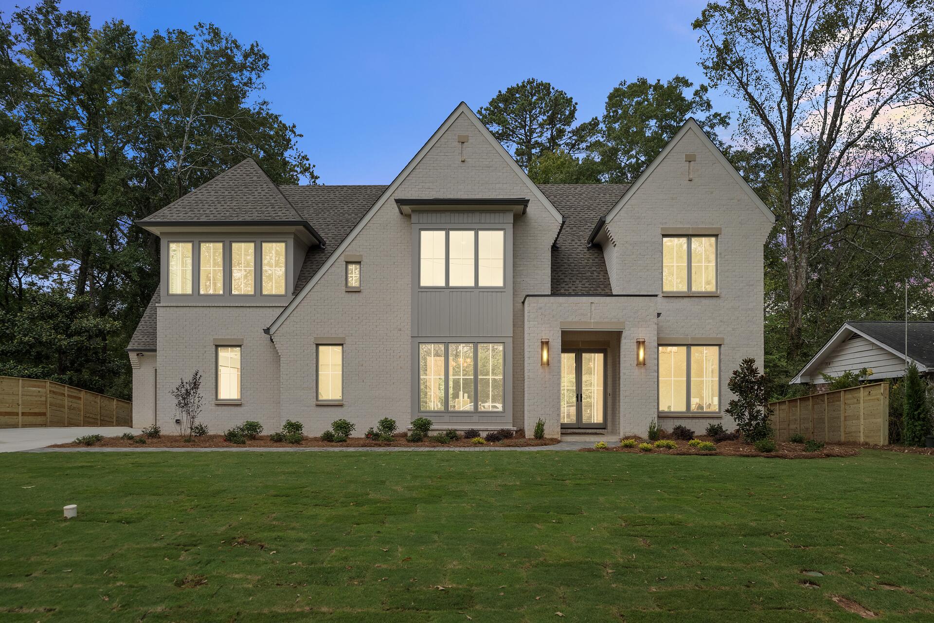A newly built home in painted brick at dusk, its windows lit, on a freshly finished lawn