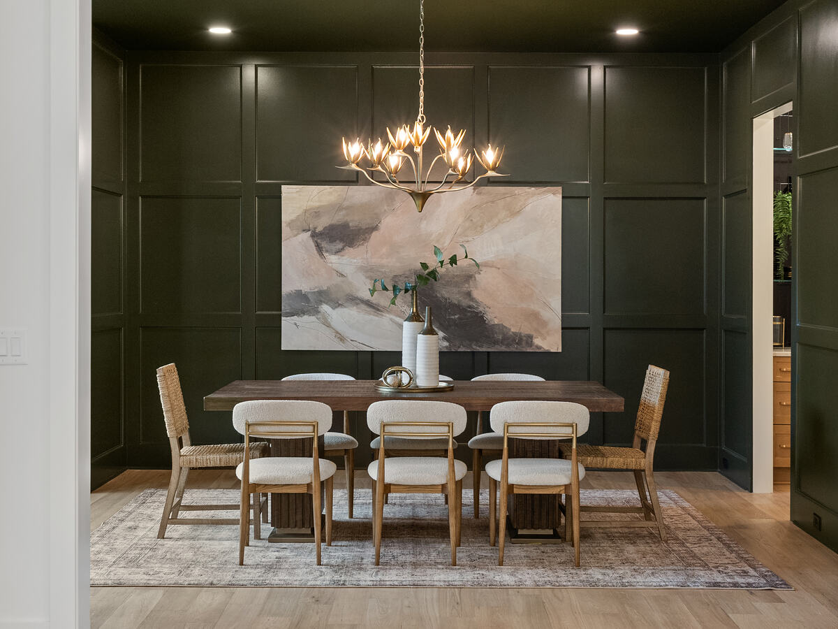 A dining room in deep green with painted paneling and a brass chandelier