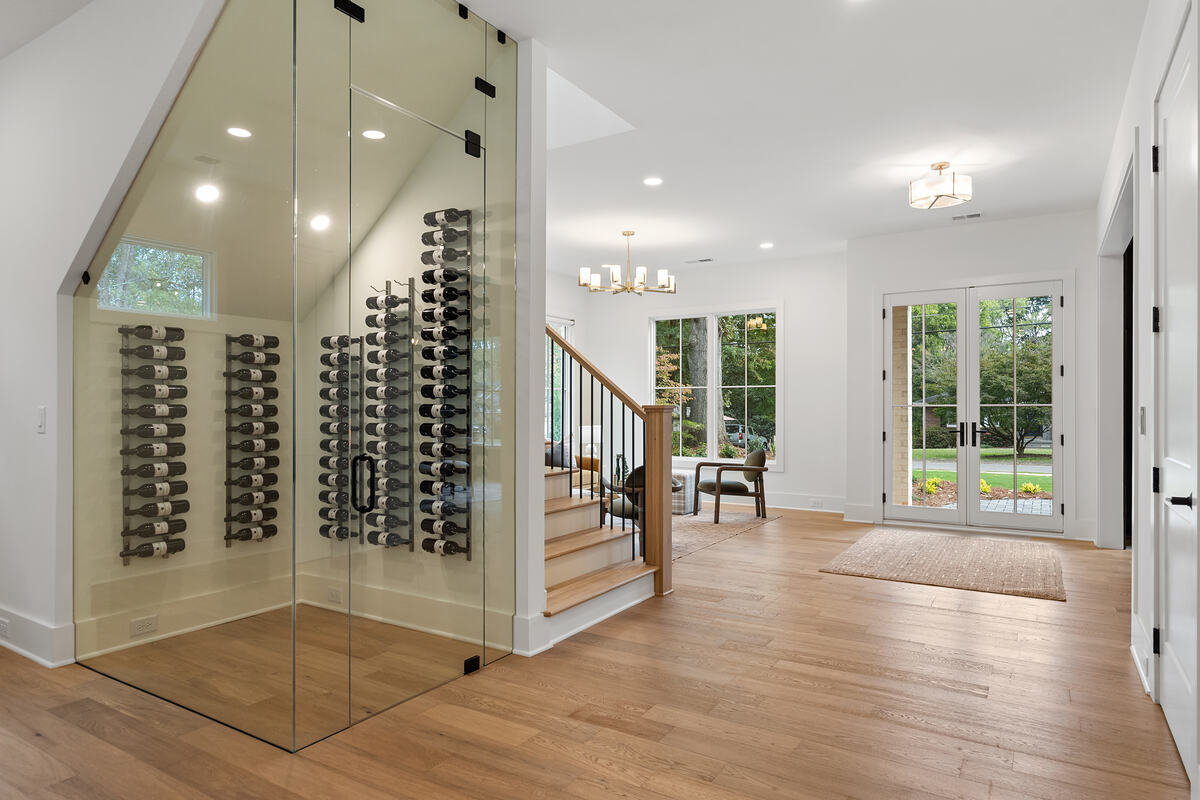 A glass-walled wine room beside the staircase in a bright entry hall