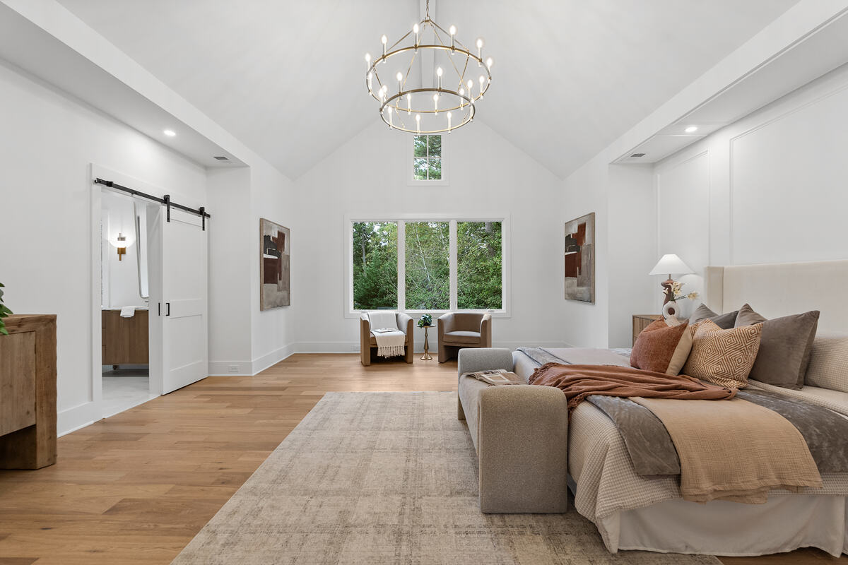 A primary bedroom with a vaulted ceiling, barn door, and wide-plank floor