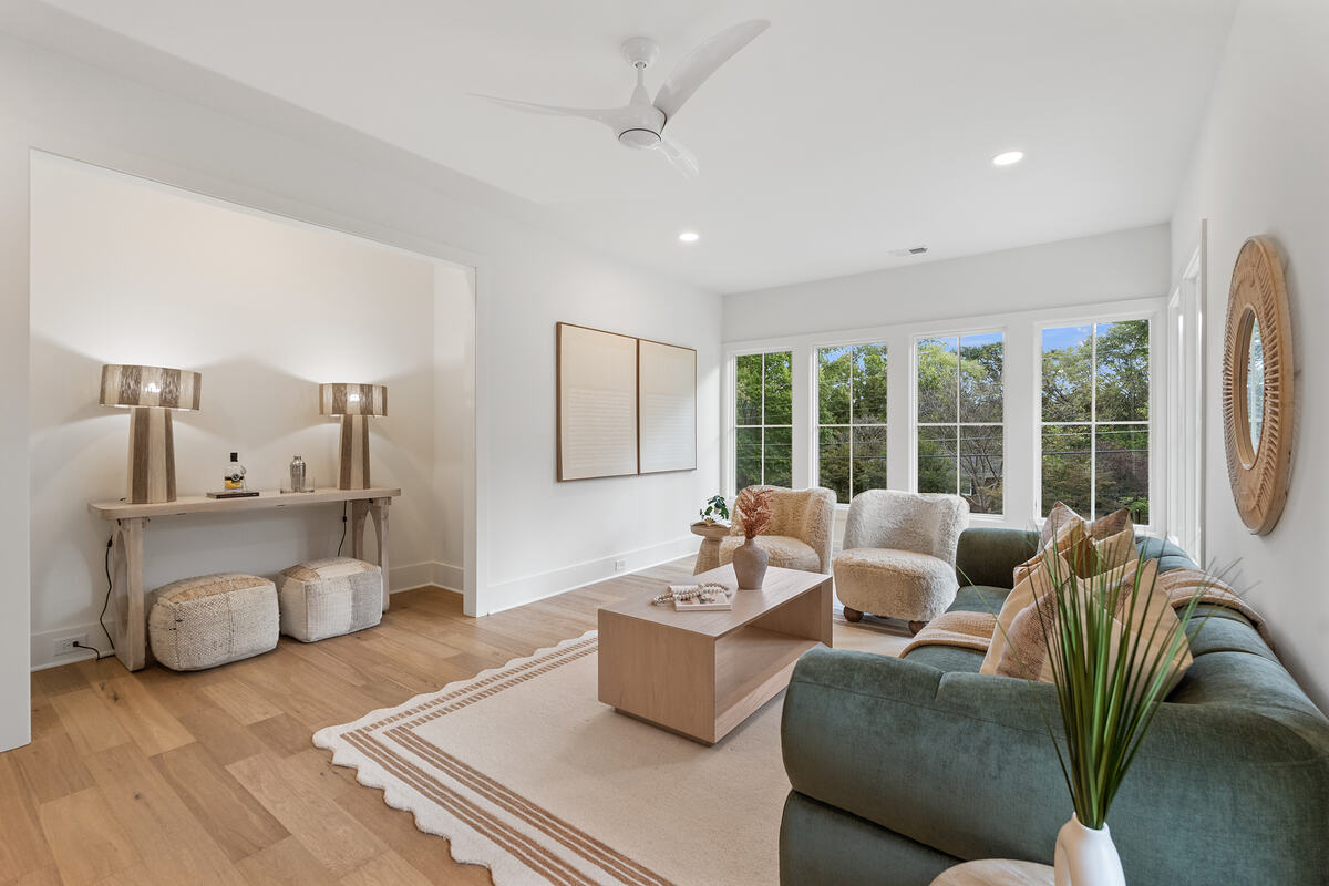 A living room with tall windows, a green sofa, and wide-plank hardwood